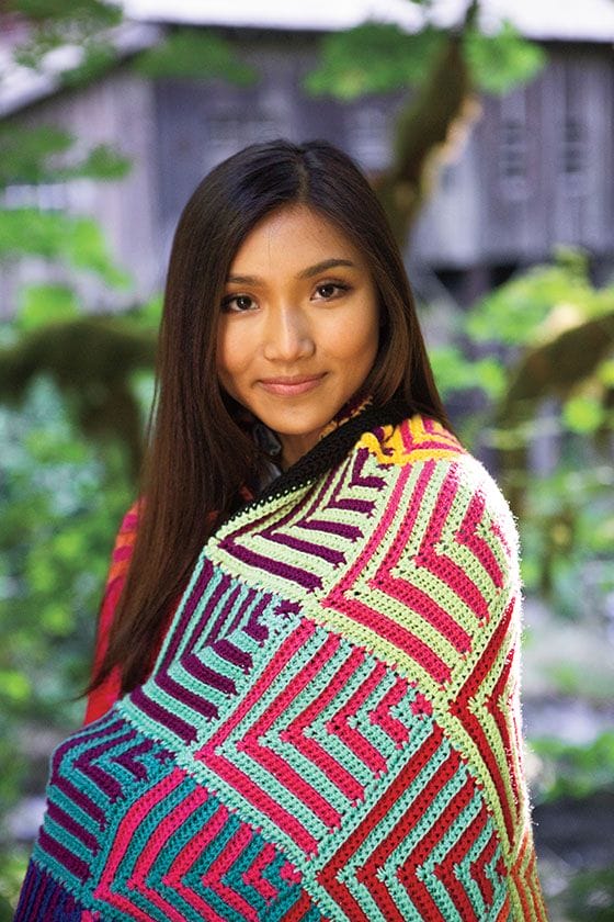 A colorful picture of a model wearing the Hue Shift Afghan around her shoulders