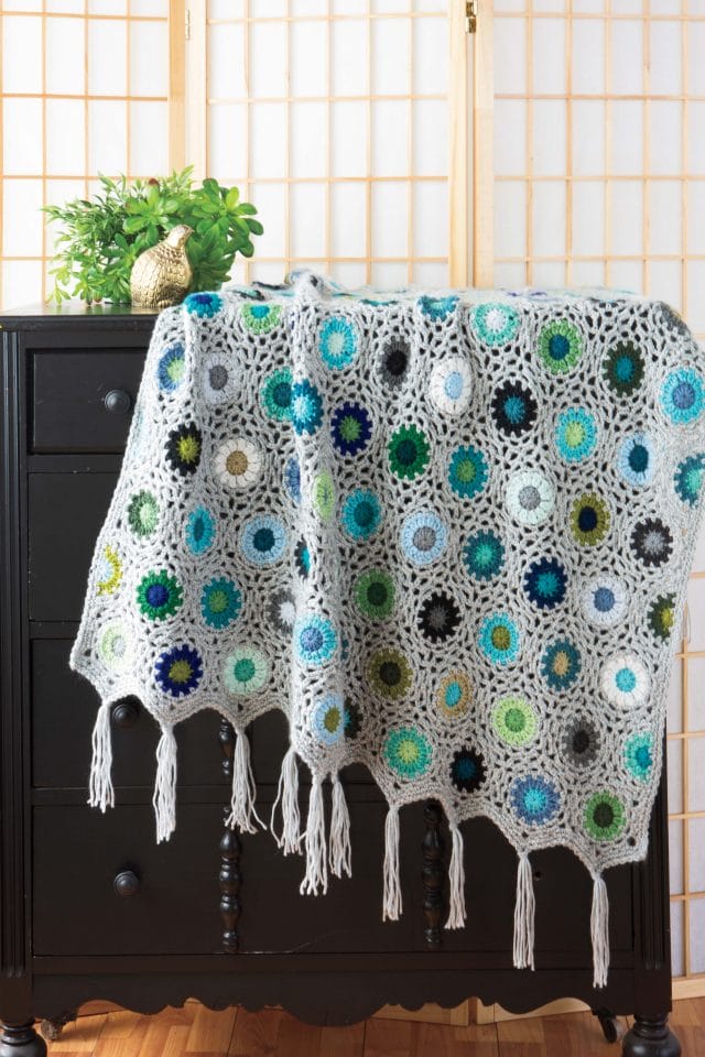 A stunning crochet blanket with multi colored round flower-like motifs is draped over a dresser.