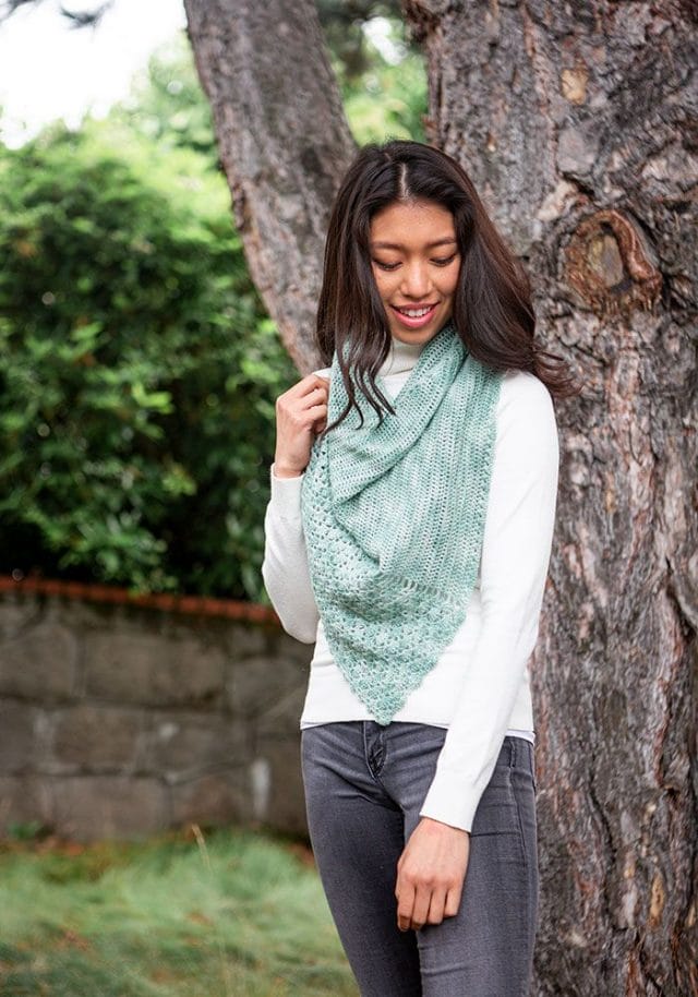 A model wears a triangular green crochet shawl draped around her neck.