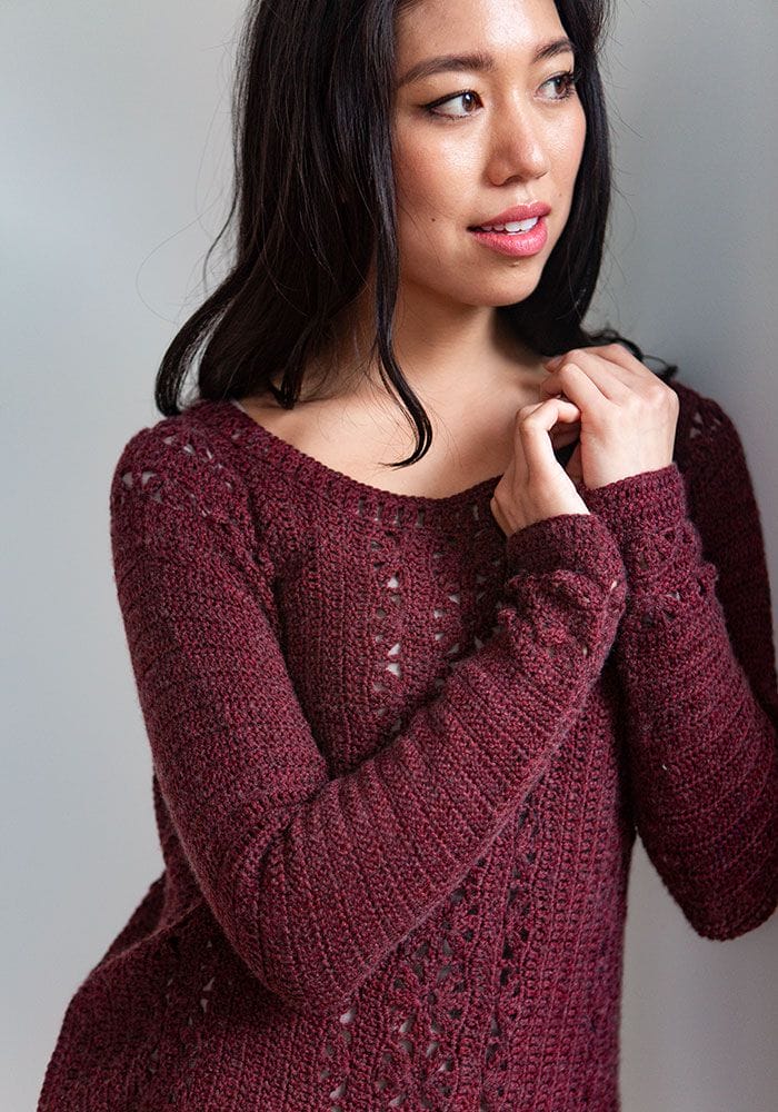 An image of a female model wearing a dark red version of the Light Touch Pullover, a free crochet pattern from crochet.com