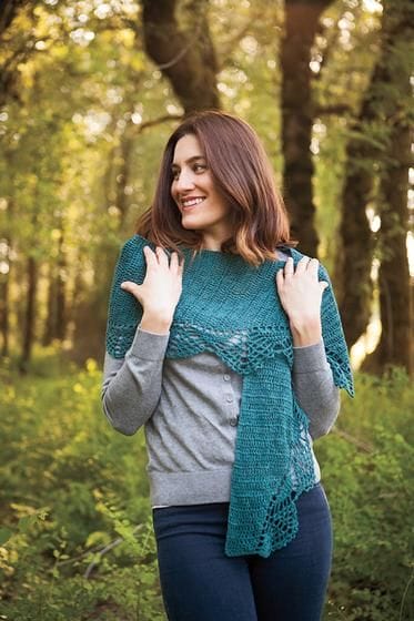 A model wears the Neasa Shawl, a turquoise crochet stole that is wrapped around her shoulders.
