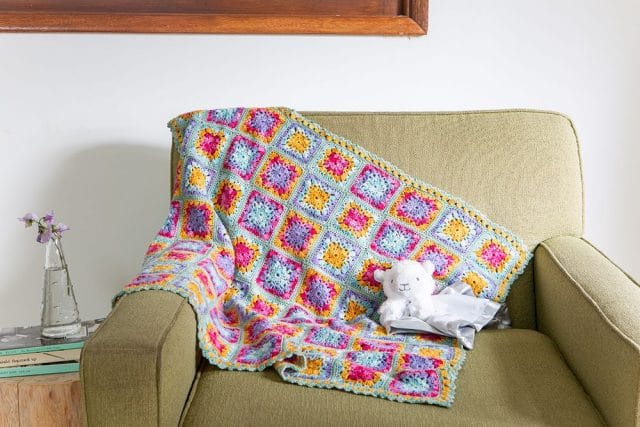 A colorful crocheted blanket is draped on a green chair