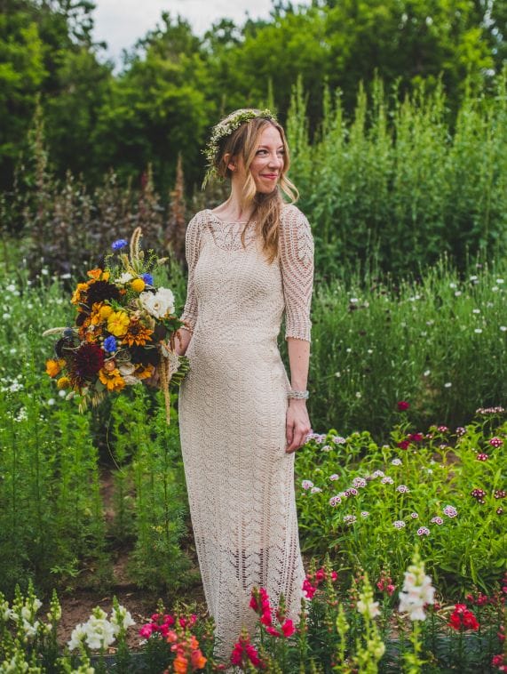 WeCrochet Brand Director Sara Dudek stands in a garden in her hand-crocheted wedding dress