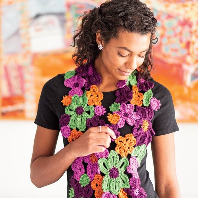 A model wears the Flower Garden Crochet Scarf, a scarf made from many colorful crocheted flowers sewn together