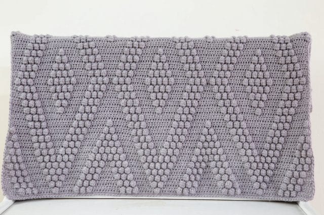 The Bobble Diamonds Throw: A gray crocheted blanket with a geometric diamond pattern made in bobble stitches