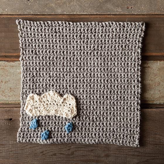 A crocheted gray dishcloth with a crocheted cloud applique and embroidered raindrops