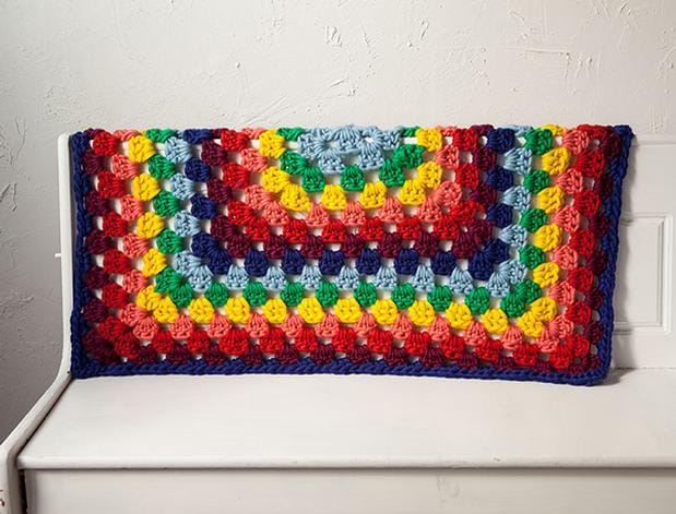 A rainbow Granny Square Blanket covers the back of a bench.