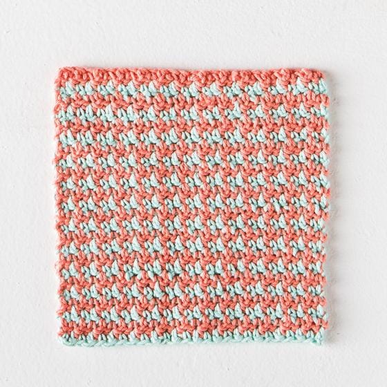 A dishcloth crocheted in peach and mint yarn with a houndstooth pattern