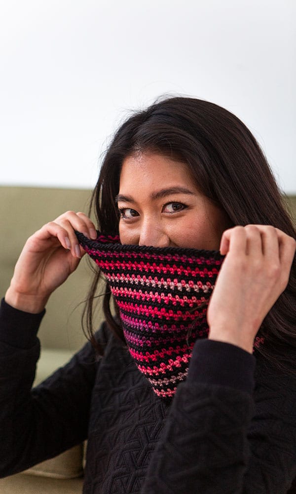 A model holds the facets cowl up over her face and smiles.