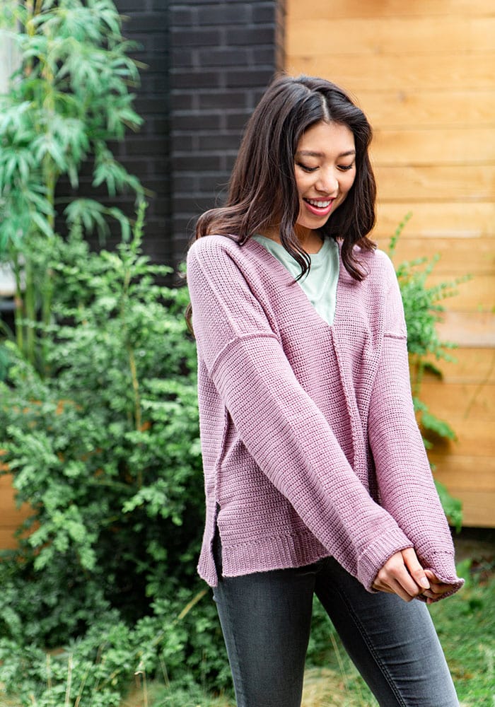 A Model wearing a crochet sweater and looking down at her sleeves. 