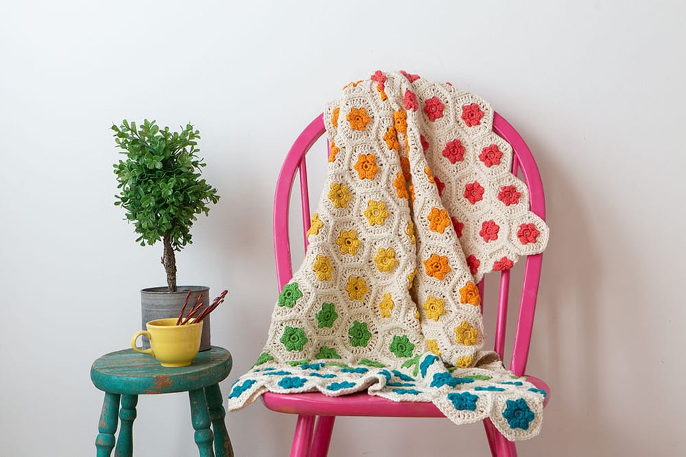 A floral, rainbow colored crocheted throw on a pink chair