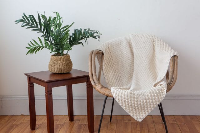 A cream-colored crocheted throw with a textural border, draped on a wicker chair