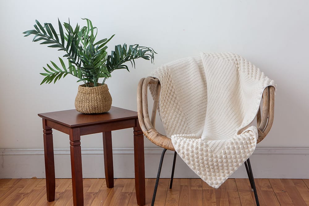 A cream-colored crocheted throw with a textural border, draped on a wicker chair