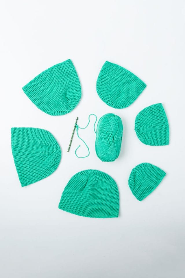 Crocheted Hats of different sizes form a circle with yarn and a crochet hook in the center.