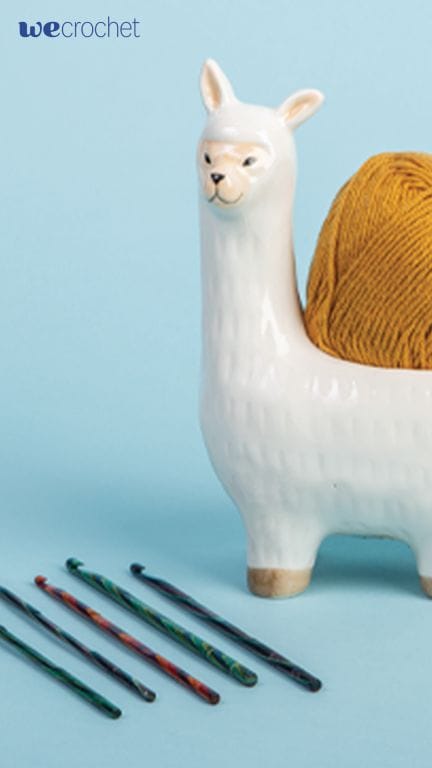 An image of an alpaca-shaped bowl holding a ball of yarn, and colorful wooden hooks lined up on the ground.