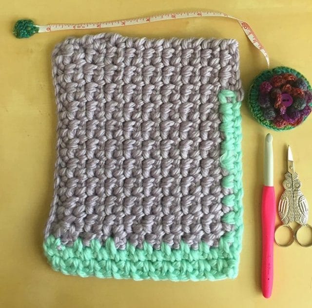 A rectangle of crochet in gray and mint next to a cute tape measure, owl-themed scissors, and crochet hook