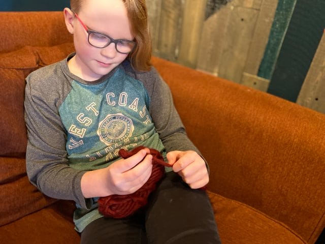 A child holds a ball of yarn and is crocheting with their fingers. One tip for crocheting with kids is to start with finger crocheting.