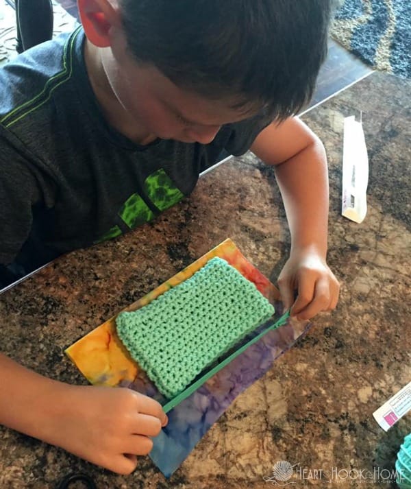 A child measures a crocheted rectangle with a zipper.