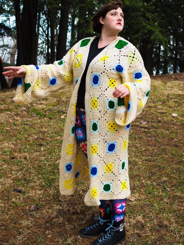 Ashley Zhong models one of her crochet blanket upcycled garments, the Softglow Granny Duster. It's made of an old cream-colored granny square afghan and has large sleeves.