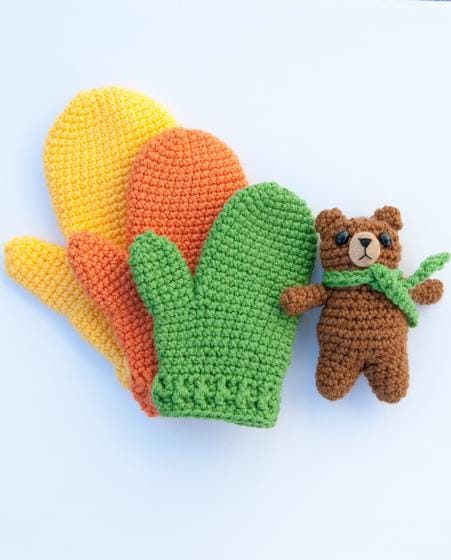 An image of 3 mittens stacked on top of each other (large, medium, small) and a small crocheted bear.