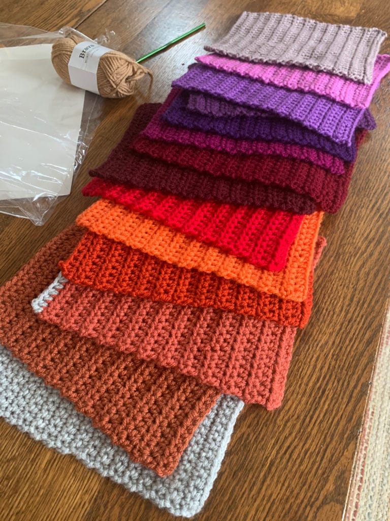 A collection of crochet rectangles spread out on the table in 14 different colors