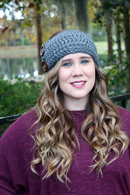 Michelle models the Amelia Earwarmer, a bulky gray crocheted headband with two large buttons on the left side.