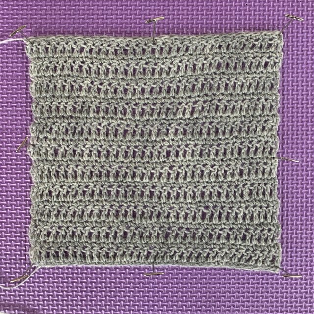 A crochet swatch on a blocking mat. Stroll in Dove Heather