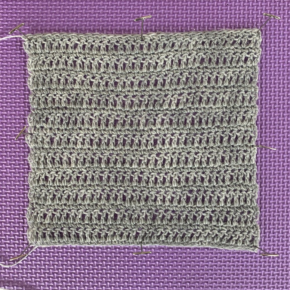 A crochet swatch on a blocking mat. Stroll in Dove Heather