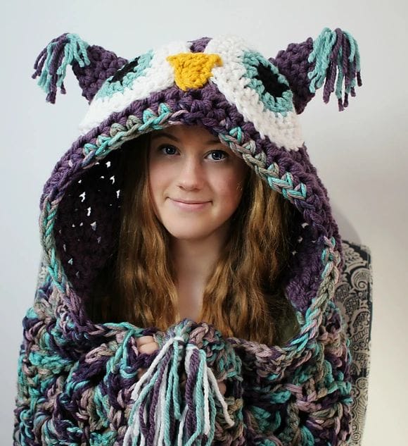 A teen girl wears a bulky crocheted hooded owl afghan