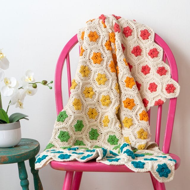 Rainbow Garden Throw: a crocheted blanket made of hexagon motifs with rainbow-colored flower blossoms in the center of each motif.