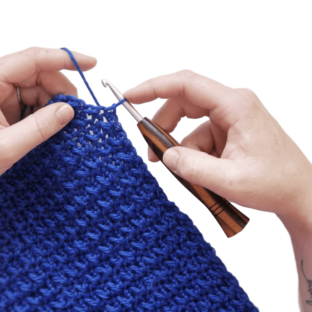 Hands crocheting a blue crochet swatch with a wooden-handled crochet hook.