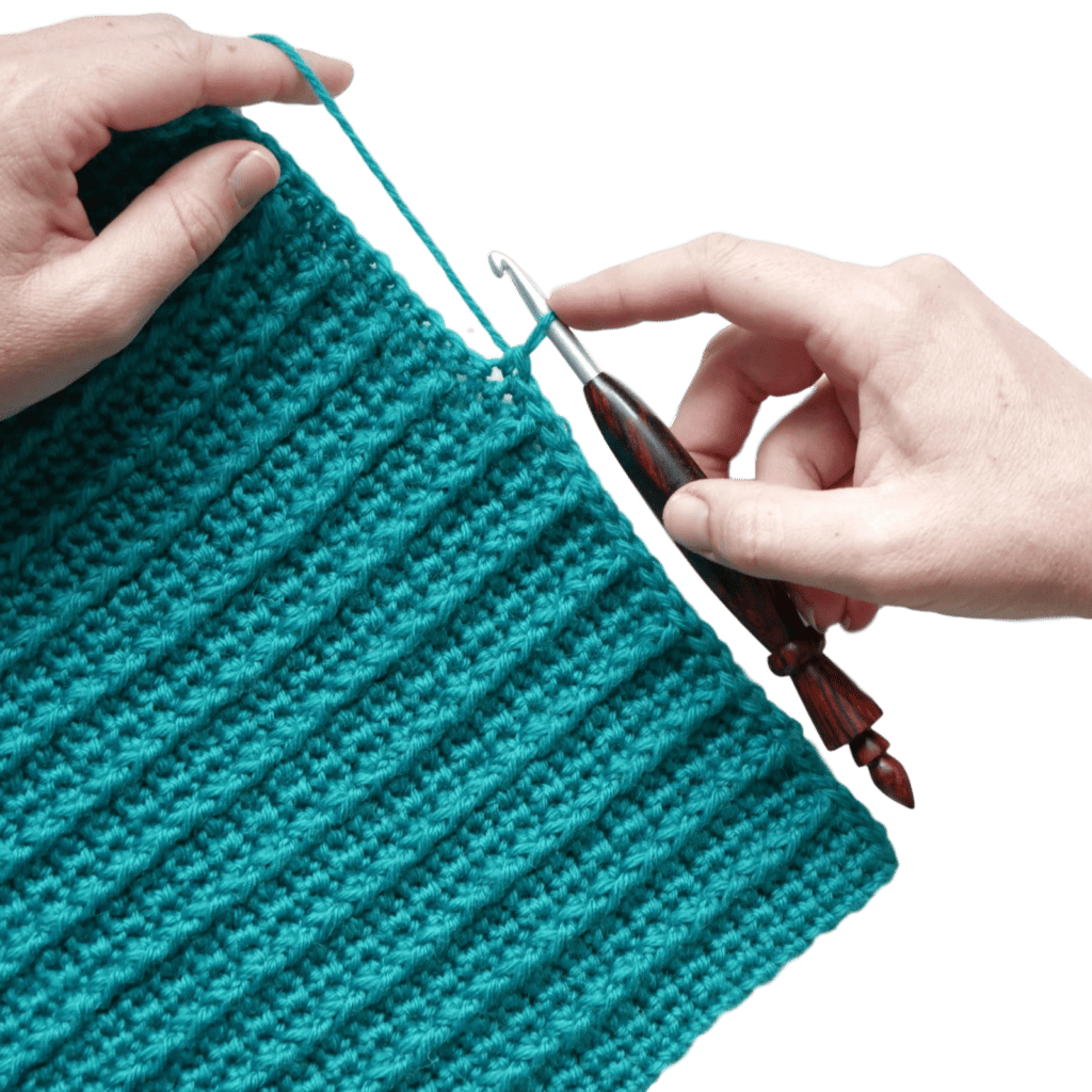 An image of hands holding a wooden crochet hook and crocheting into a turquoise crocheted swatch with vertical lines of front post double crochet spanning up and down the swatch.