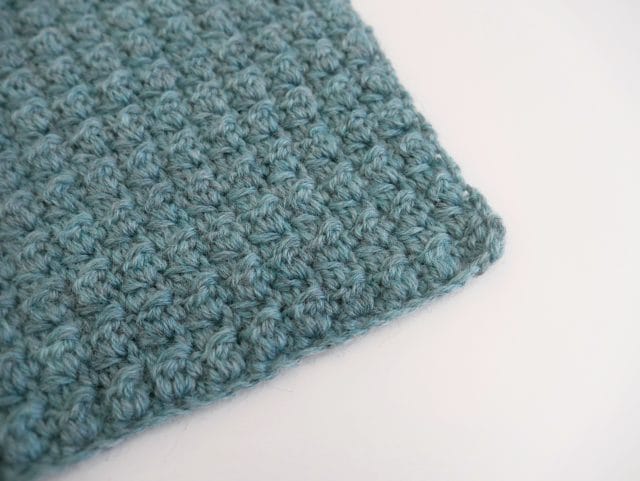 The corner of a greenish-blue textured crochet swatch on a white background.