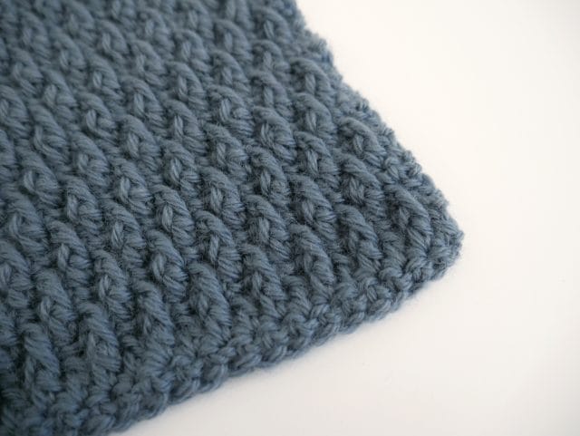 The corner of a blue-gray crochet swatch with nubby texture on a white background.