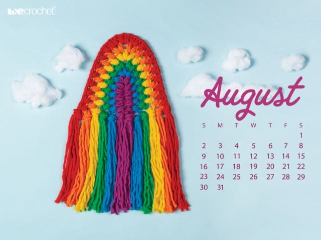 On a sky-blue background, a crocheted rainbow wall hanging, reminiscent of macrame, in rainbow colored puff stitches: red, orange, yellow, green, blue, purple. In the background, clouds made of cotton batting. On the left, an August 2020 calendar in purple.