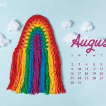 On a sky-blue background, a crocheted rainbow wall hanging, reminiscent of macrame, in rainbow colored puff stitches: red, orange, yellow, green, blue, purple. In the background, clouds made of cotton batting. On the left, an August 2020 calendar in purple.