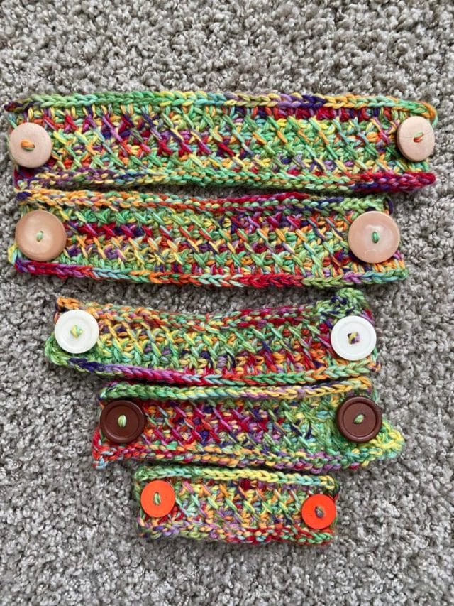 A top-down view of crocheted ear savers in graduated sizes, starting from longest and descending to the shortest length, made in multicolored yarn.