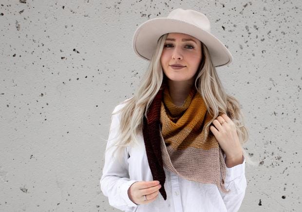 A woman wears a multicolored brown-toned crocheted shawl wrapped around her neck.