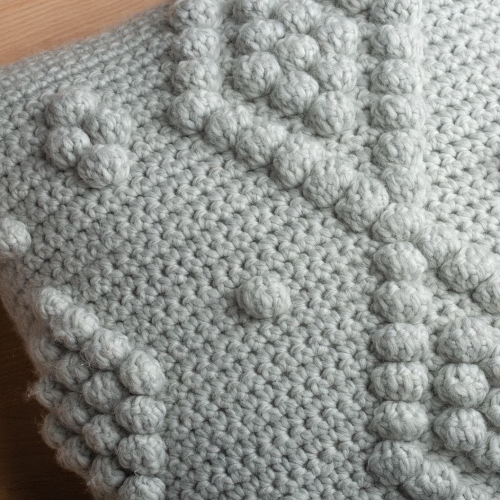 Closeup of crochet texture in gray featuring bobble stitches in a diamond formation. One of our free home decor crochet patterns.