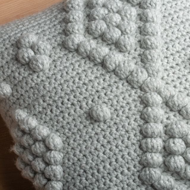 Closeup of crochet texture in gray featuring bobble stitches in a diamond formation. One of our free home decor crochet patterns.