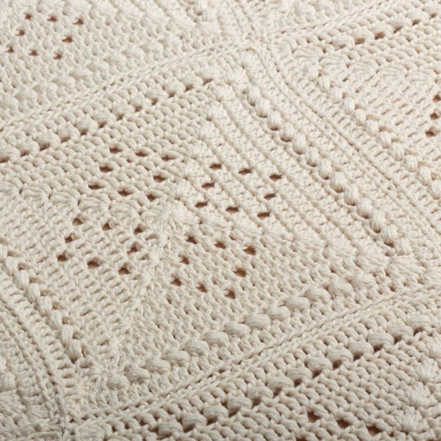 closeup of a crocheted blanket in off white with a diamond pattern on it