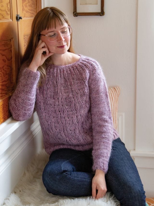 A model wears a pink fuzzy cabled crochet sweater