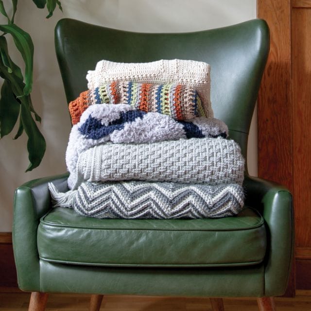 A stack of folded crocheted blankets on a stylish green chair