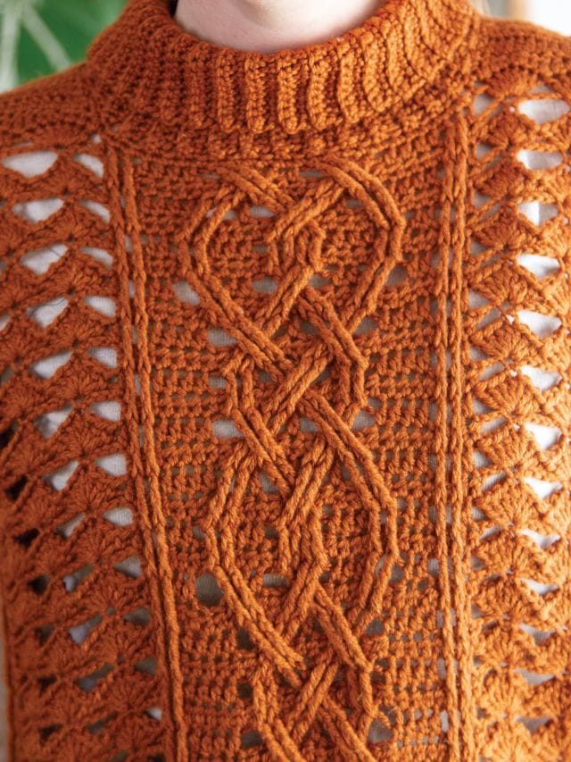 A close up of the crochet cable stitches of the Midtown Mantle Mock-Neck Top, made in a copper colored yarn.