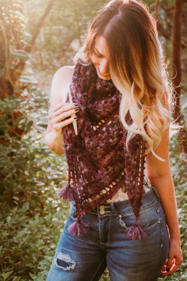 Picot Crochet Shawl pattern by Briana K Designs. A model wears a large plum-colored crocheted shawl around her neck. It has fuzzy tassels at its points.
