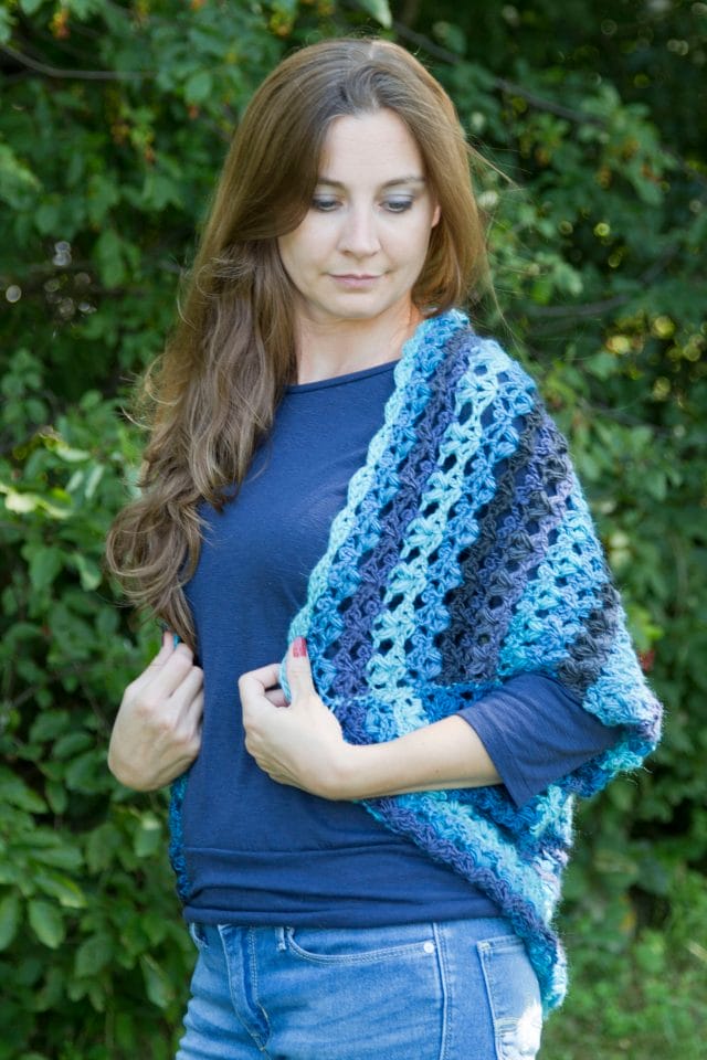KoKo Cocoon Cardigan by Crystalized Designs. A model wears a gradient blue crocheted shrug.