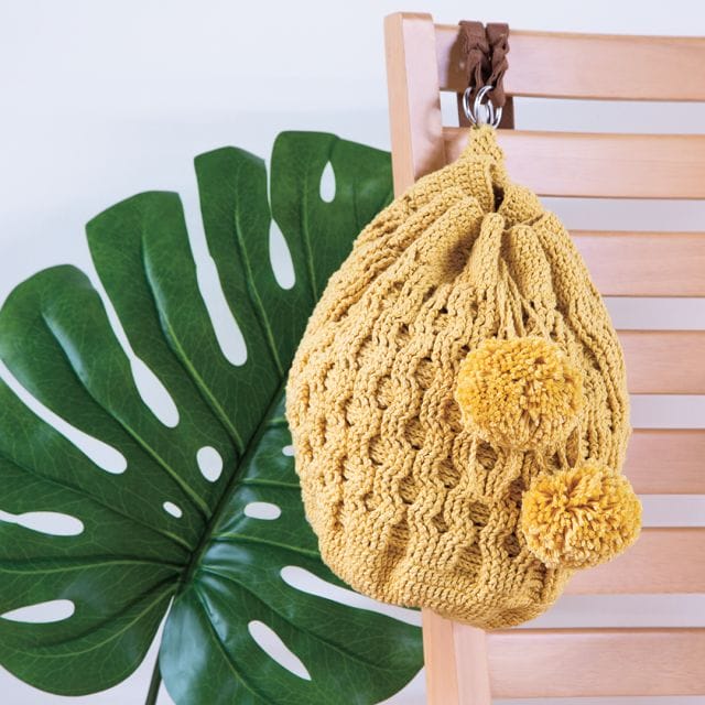 A cable crocheted yellow backpack with big pom-poms