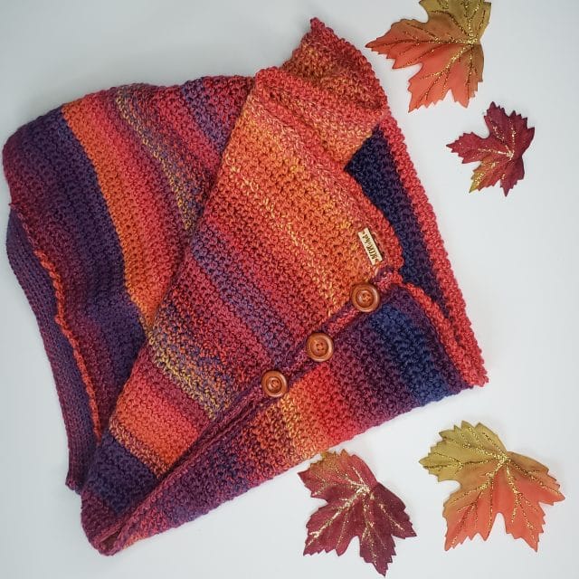Boxed In crochet shrug pattern by ACCROchet. A top-down view of the Boxed In shrug - it has a sunset colored gradient thanks to Chroma Twist yarn, and is surrounded by sparkly fall leaves.