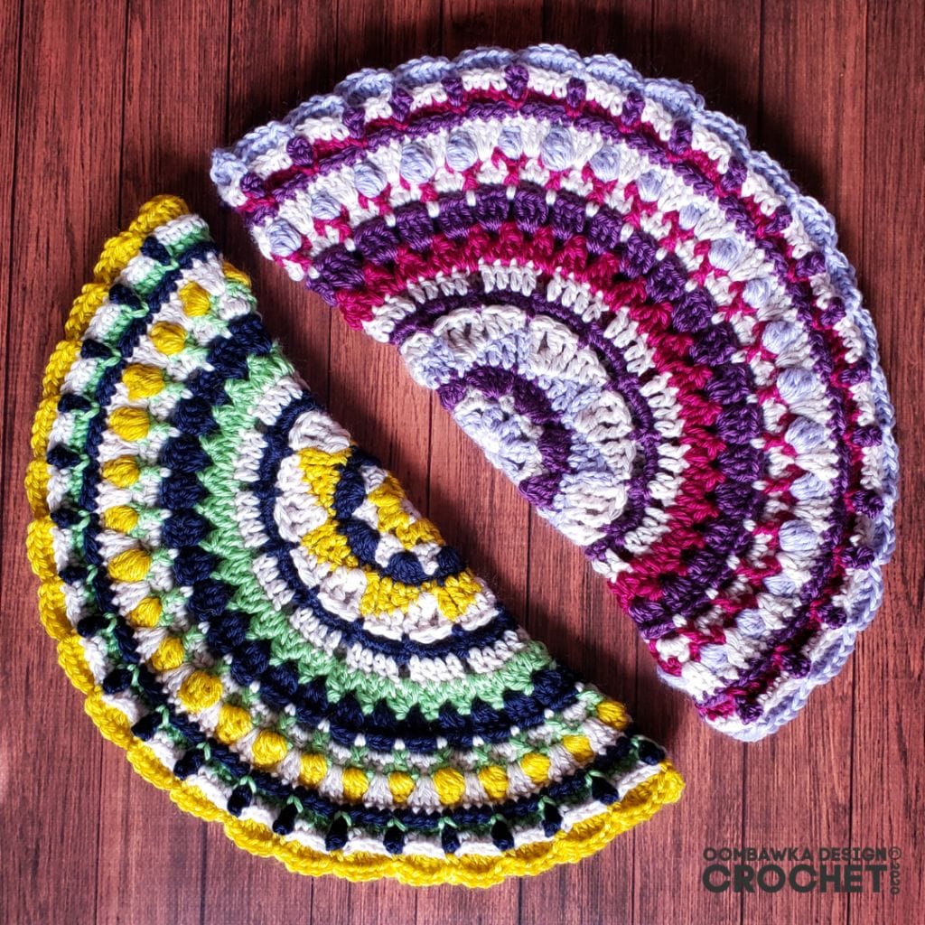 September Mandala by Oombawka Design Crochet. Folded in half, a crocheted mandala made in layers of tan, navy, yellow, and spring green. Next to it, another half mandala in cream, purple, magenta, and lavender.