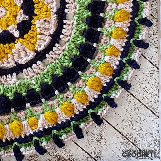 September Mandala by Oombawka Design Crochet. The corner of a round crocheted mandala made in layers of tan, navy, yellow, and spring green.